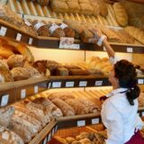 Eine Verkäuferin beim Bäcker greift in ein Brot-Regal.
