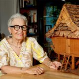 Marianne Telgmann aus Kamen sitzt neben dem Modell eines traditionellen indonesischen Hauses.