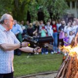 Burkhard Böhnisch steht mit einem Flammenwerfer in der Hand im Kurpark in Unna. Mit dem Gerät zündet er einen großen Holzstapel an. Im Hintergrund sind die Besucher des Mittsommernachtsfestes 2024 zu sehen.