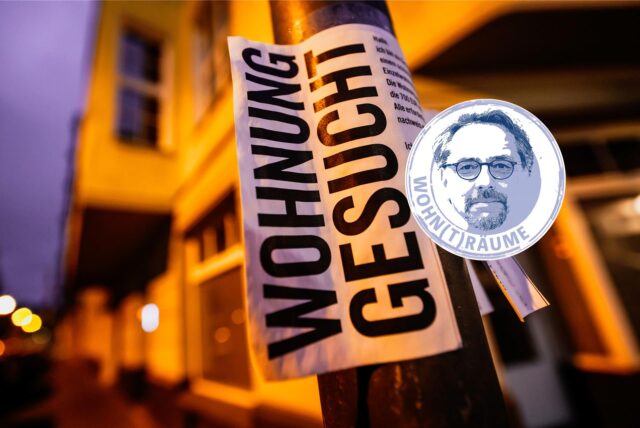 Ein Zettel mit der Aufschrift „Wohnung gesucht“ hängt vor Wohnhäusern.