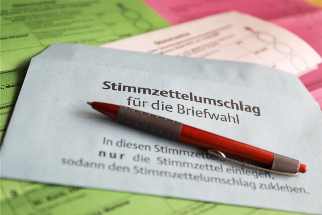 Stimmzettel und ein Umschlag für die Briefwahl liegen auf dem Tisch.
