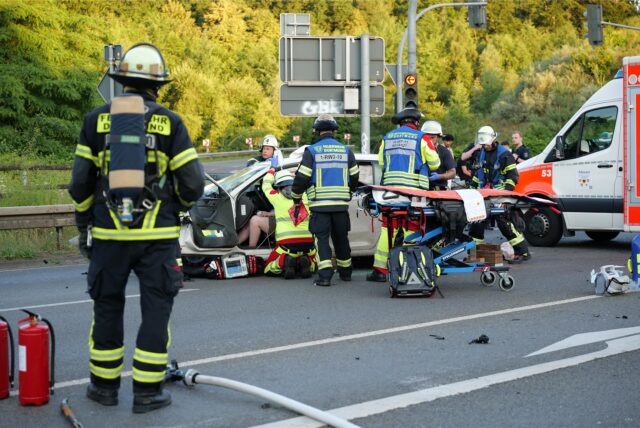 Einsatzkräfte der Feuerwehr Dortmund sind am Unfallort eingetroffen und kümmern sich um die Bergung einer verletzten Person aus einem Pkw. Ein Rettungswagen steht bereit, um die Person zu versorgen.