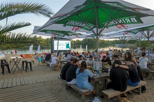 Viele Besucher sitzen am Horstmarer See am Strand vor einer Leinwand.