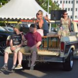 Eine Gruppe Menschen sitzt auf der Ladefläche eines alten Pick Ups.