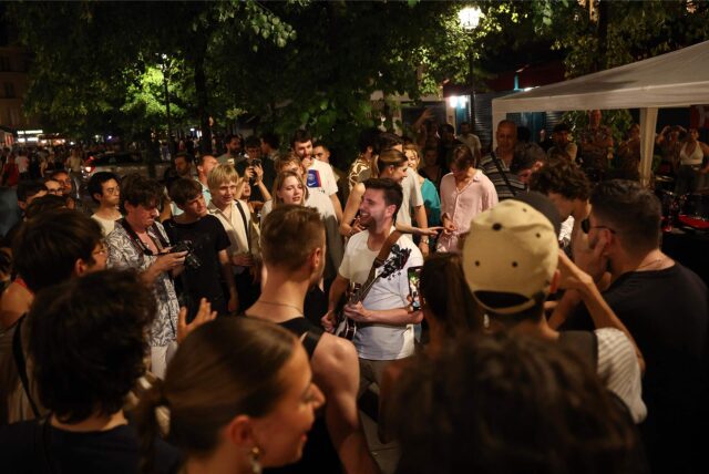 Musikbegeisterte lauschen einem Mann, der während des jährlichen französischen Straßenmusikfestivals „Fete de la Musique“ im 4. Arrondissement von Paris Gitarre spielt.