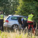 Ein silbernes Auto steht vor einem Baum, Einsatzkräfte schauen es sich genauer an.