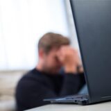 Ein Mann sitzt mit den Händen vor dem Gesicht verzweifelt hinter einem Laptop.