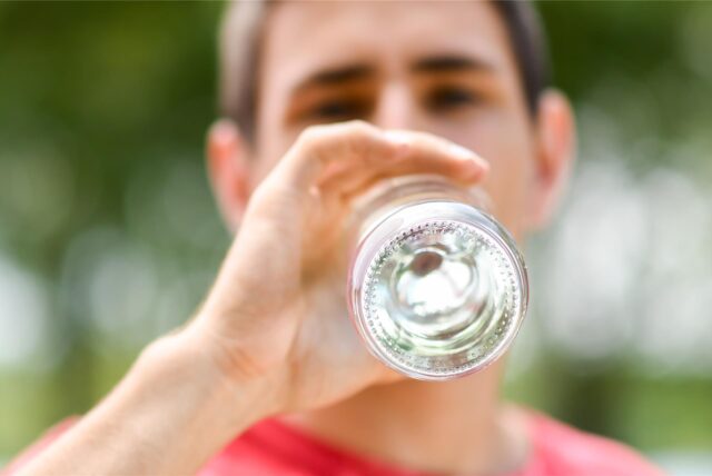 Ein Mann trinkt stilles Mineralwasser aus einer Glasflasche.