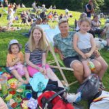 Menschen sitzen im Römerpark beim Kulturpicknick auf Decken und Klappstühlen und essen.