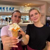 Dahlia Beck und Lara Bilinsky, Mitarbeiterinnen des Eisdiele Venezia in Kamen, halten eine Waffel Eis mit einer Kugel Joghurt-Orange in den Händen.