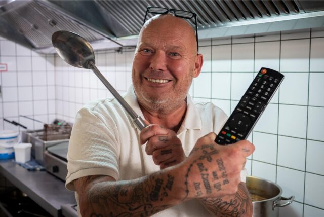 Gastronom Dirk Lasarz steht mit einer Kelle und einer Fernsehfernbedienung in der Küche des Kaiserhofs.