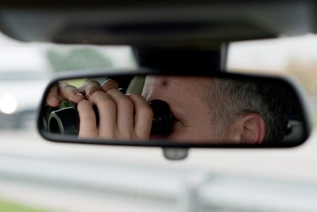 Ein Mann sitzt in einem Auto und schaut durch ein Fernglas.