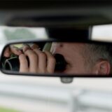 Ein Mann sitzt in einem Auto und schaut durch ein Fernglas.