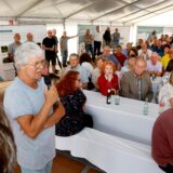 Bernhard Salfer spricht in ein Mikrofon, während ihm Menschen im gut besuchten Zelt zuhören.