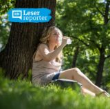 Symbolbild zu Hitze in Dortmund: Eine Frau sitzt im Schatten unter einem Baum und trinkt Wasser