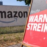 Ein Amazon-Logo ist auf einem Zaun im Hintergrund zu sehen. Im Vordergrund steht ein Schild mit der Aufschrift „Heute Warnstreik“.