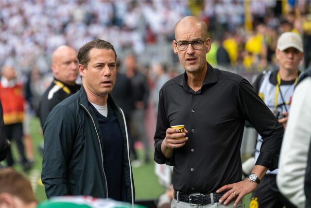 Lars Ricken steht neben Carsten Cramer, der einen Kaffeebecher in seiner rechten Hand hält.