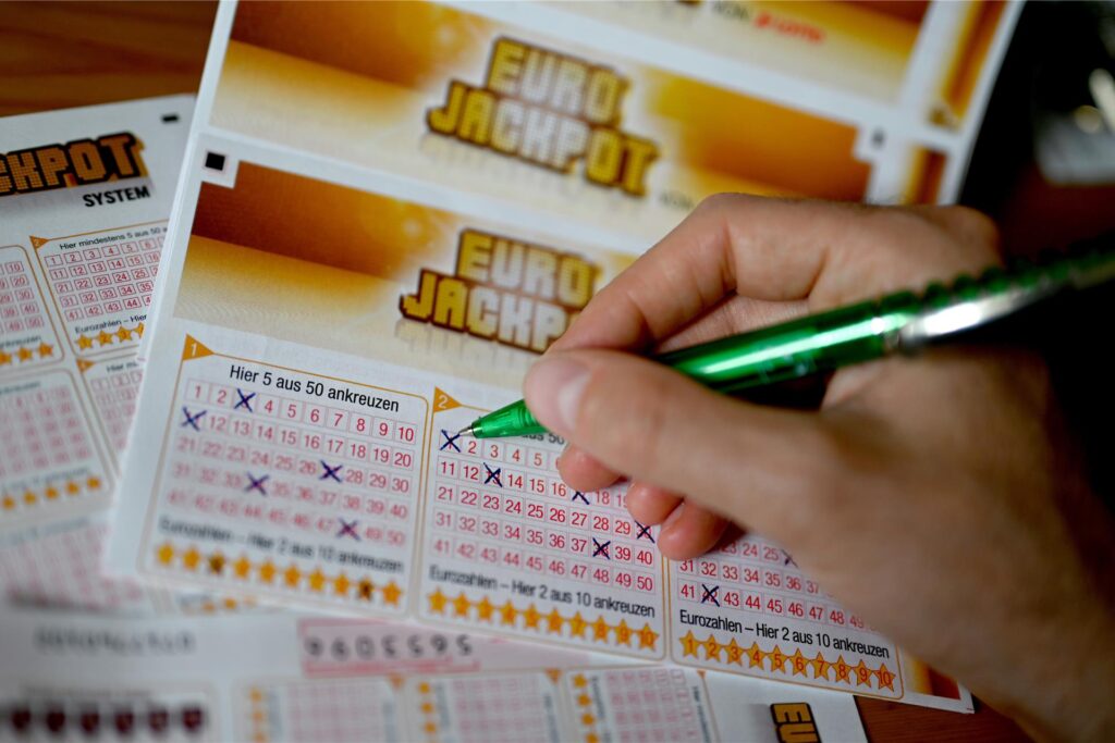 Eine Person füllt mit einem Kugelschreiber einen Eurojackpot-Schein aus - ein paar Gewinnzahlen und Eurozahlen wurden bereits angekreuzt. Eine Person füllt mit einem Kugelschreiber einen Eurojackpot-Schein aus - ein paar Gewinnzahlen und Eurozahlen wurden bereits angekreuzt.
