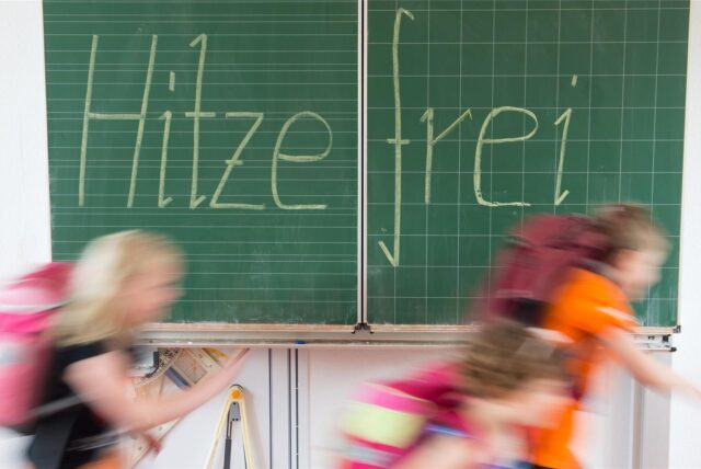 Schüler einer 2. Klasse laufen in einer Grundschule an einer Tafel mit der Aufschrift „Hitzefrei“ vorbei.