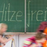 Schüler einer 2. Klasse laufen in einer Grundschule an einer Tafel mit der Aufschrift „Hitzefrei“ vorbei.