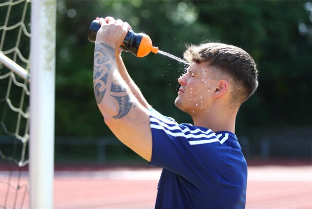 Ein Fußballer erfrischt sich, indem er sich Wasser aus einer Trinkflasche ins Gesicht spritzt
