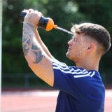 Ein Fußballer erfrischt sich, indem er sich Wasser aus einer Trinkflasche ins Gesicht spritzt