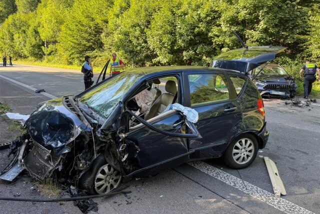 Zwei Autos stehen nach einem Unfall auf der B54 in Hagen auf der Straße. Polizisten untersuchen die Unfallstelle.