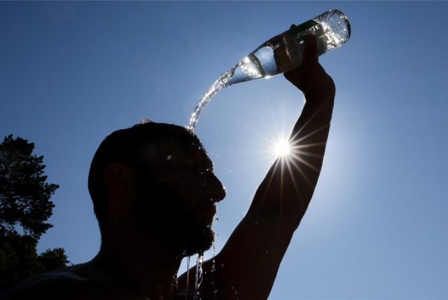 Ein Mann kühlt sich bei sommerlichen Temperaturen ab, in dem er sich eine Flasche mit Wasser über den Kopf schüttet.
