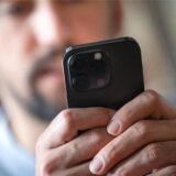 Ein Mann hält ein schwarzes Smartphone in der Hand.