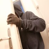 Eine Person mit Handschuhen und Kapuze öffnet eine weiße Wohnungstür.