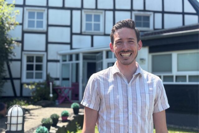 Dario Roßbach steht vor seiner Praxis in Schwerte-Villigst. Der Zahnarzt lächelt fröhlich in die Kamera.