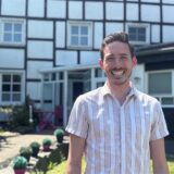 Dario Roßbach steht vor seiner Praxis in Schwerte-Villigst. Der Zahnarzt lächelt fröhlich in die Kamera.
