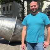 Christian Hüther steht auf dem Postplatz in Schwerte. Er trägt ein blaues T-Shirt und Jeans. Hinter ihm ist die Brunnenskulptur zu sehen.