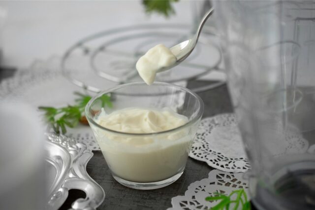 Ein Glas mit Joghurt und ein Löffel, mit dem offenbar gerade Joghurt aus dem Glas entnommen wurde.