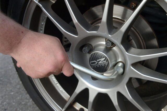 Ein Mann benutzt einen Radmutternschlüssel, um die Radmuttern eines Autorades mit einer silbernen OZ Racing Felge festzuziehen. Die Bremsscheibe ist im Hintergrund sichtbar.