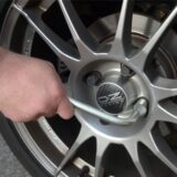 Ein Mann benutzt einen Radmutternschlüssel, um die Radmuttern eines Autorades mit einer silbernen OZ Racing Felge festzuziehen. Die Bremsscheibe ist im Hintergrund sichtbar.