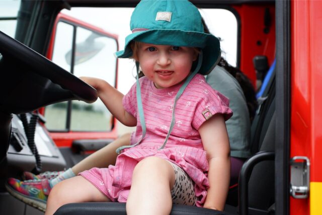 Ein junges Kind sitzt am Lenkrad eines Feuerwehrwagens.