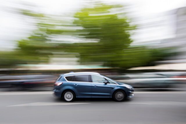 Ein blaues Auto fährt mit hoher Geschwindigkeit auf einer Straße. Das Tempo wird durch die Bewegungsunschärfe des Bildes sichtbar.
