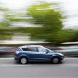Ein blaues Auto fährt mit hoher Geschwindigkeit auf einer Straße. Das Tempo wird durch die Bewegungsunschärfe des Bildes sichtbar.