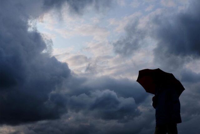 Ein Mann geht mit einem Regenschirm vor aufziehenden dunklen Wolken spazieren.