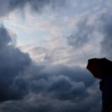 Ein Mann geht mit einem Regenschirm vor aufziehenden dunklen Wolken spazieren.