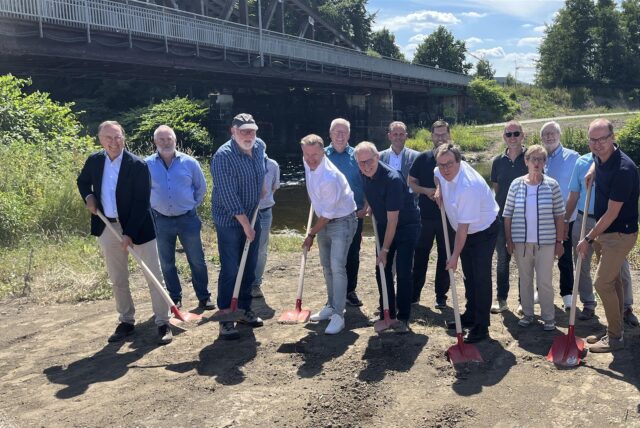 Viele Beteiligte des Brückenneubaus in Wickede stehen mit Spaten an der Baustelle