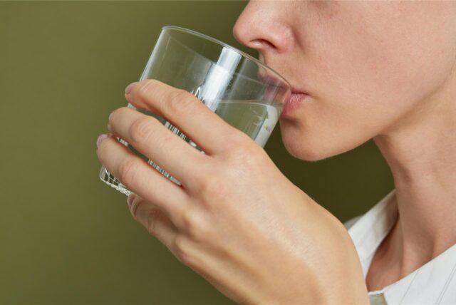 Eine Frau hält sich ein Wasserglas an den Mund.