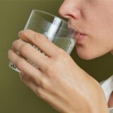 Eine Frau hält sich ein Wasserglas an den Mund.