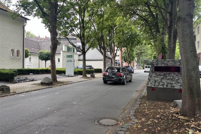 Auf der Goethestraße in Schwerte steht am Fahrbahnrand in einem Beet der Superblitzer des Kreises Unna. Ein schwarzes Auto passiert ihn in Fahrtrichtung Rathaus.