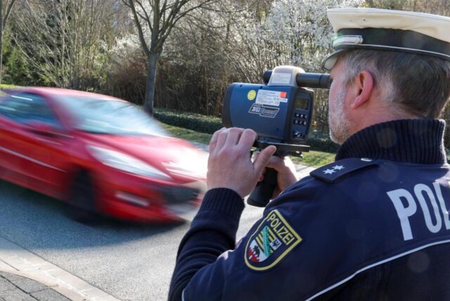Polizist mit Radarpistole misst die Geschwindigkeit eines vorbeifahrenden Autos.