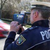 Polizist mit Radarpistole misst die Geschwindigkeit eines vorbeifahrenden Autos.