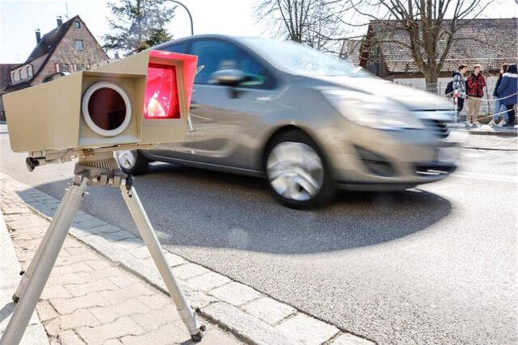 Mobiler Blitzer misst Geschwindigkeit eines vorbeifahrenden Autos in einer Ortschaft Mobiler Blitzer misst Geschwindigkeit eines vorbeifahrenden Autos in einer Ortschaft
