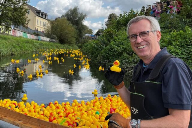 Stefan Ellinghaus vom Rotary-Club Kamen fischt eine Ente aus dem Wasser der Seseke. Auf dem Wasser schwimmen mehrere gelbe Plastik-Enten.
