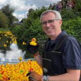 Stefan Ellinghaus vom Rotary-Club Kamen fischt eine Ente aus dem Wasser der Seseke. Auf dem Wasser schwimmen mehrere gelbe Plastik-Enten.